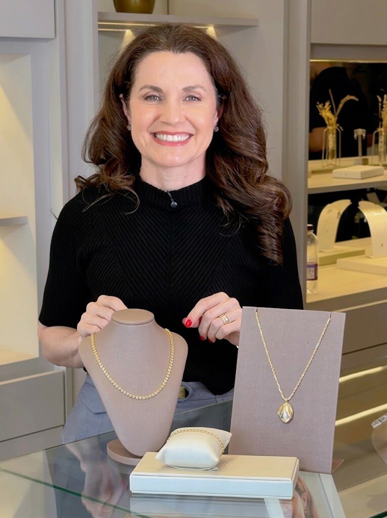 Cris apresentando colares e pulseiras douradas no balcão da loja